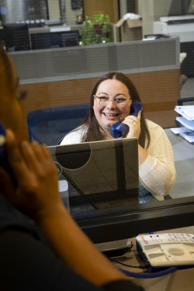 Two people on opposite sides of clear screen talking to each other through telephone