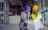 Two men in construction hats looking at large piece of paper